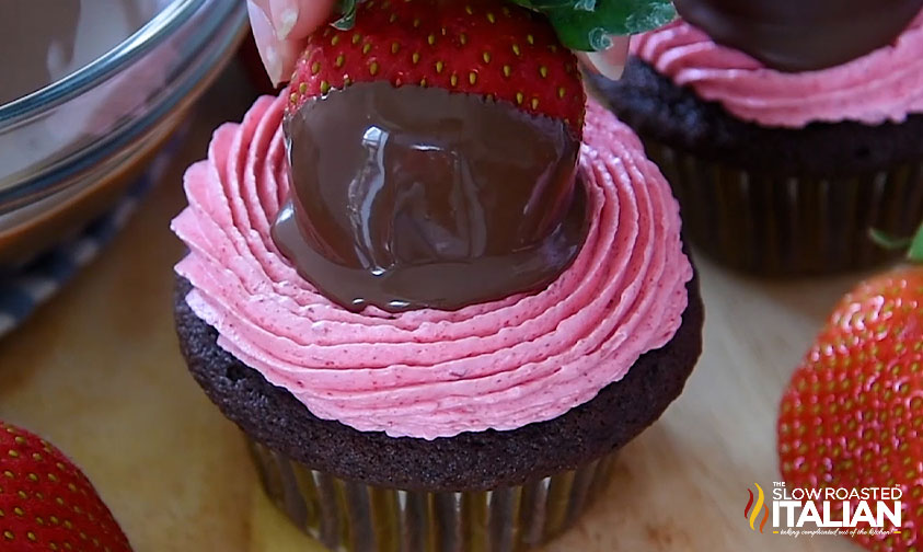 placing chocolate dipped strawberry on cupcake