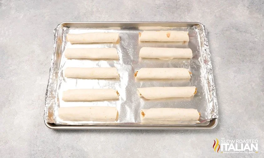 beef wrapped in flour tortillas on foil-lined sheet pan, ready for baking