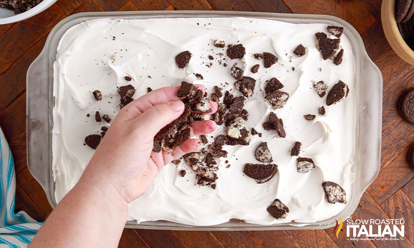 sprinkling crushed oreos on top of oreo lasagna