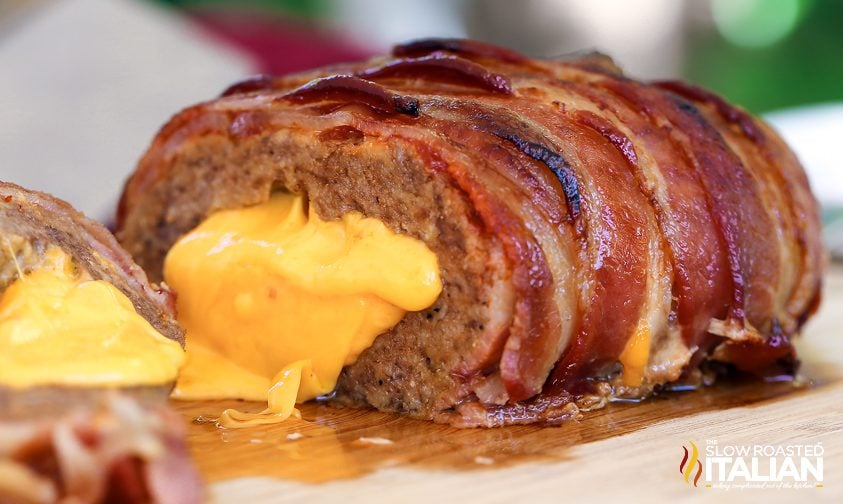 ground beef meatloaf stuffed with cheese and wrapped with bacon on a cutting board