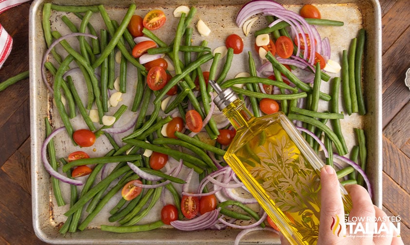 drizzling olive oil over fresh vegetables on sheet pan.