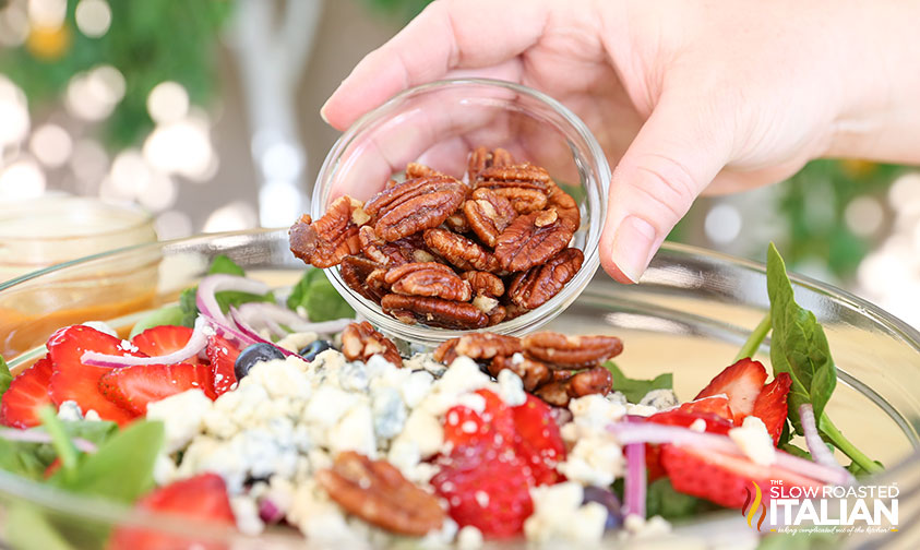 adding candied pecans to vegetables in bowl