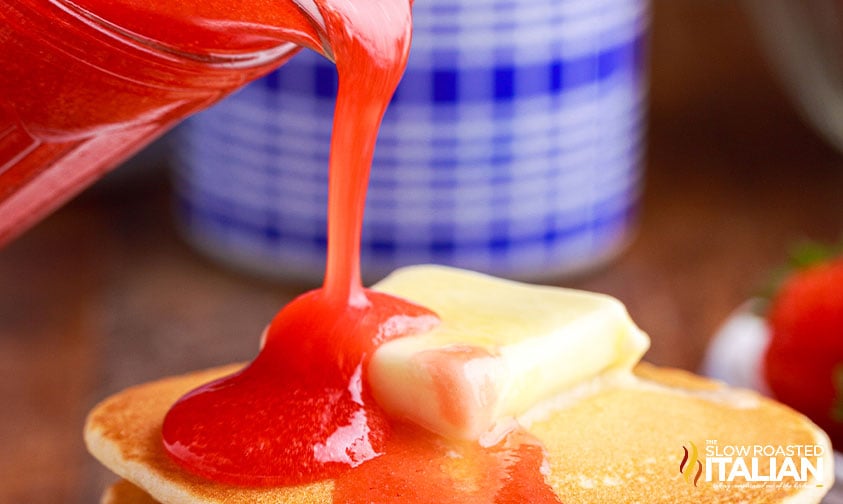 pouring strawberry pancake syrup on buttered pancake, closeup