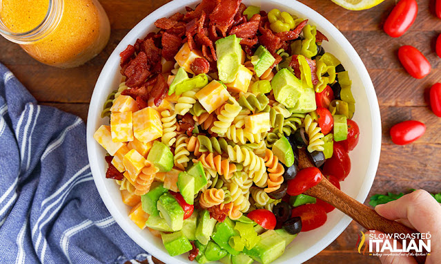 overhead: bowl of crumbled bacon, colby cheese cubes, avocado, black olive slices and diced tomatoes