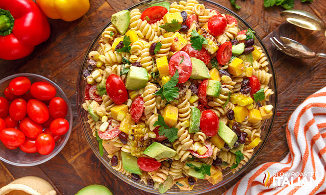 overhead: bowl of corn and black bean salad with rotini, avocado, cherry tomatoes and cheddar cheese cubes