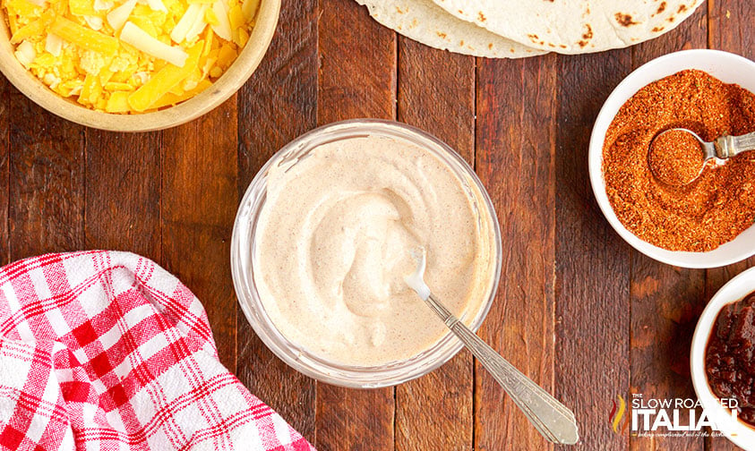 creamy chipotle sauce in a clear bowl next to beef quesarito ingredients