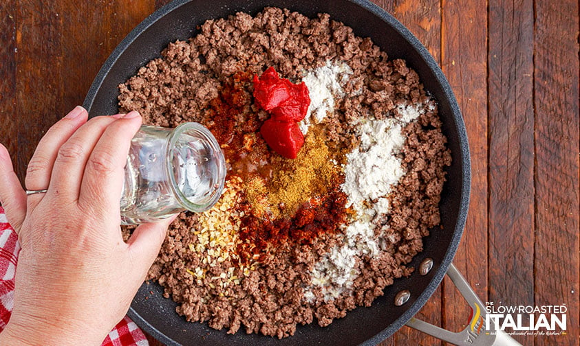 pouring water into skillet of cooked ground beef and seasoning