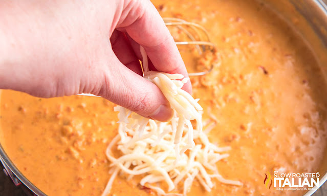 adding shredded mozzarella cheese to creamy sauce in a skillet
