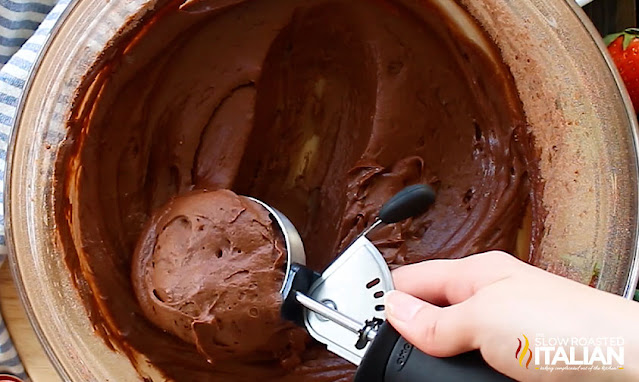 scooping thick chocolate batter from mixing bowl