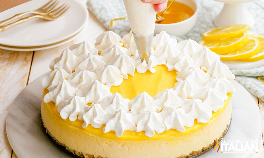 piping whipped cream onto top of baked lemon cheesecake