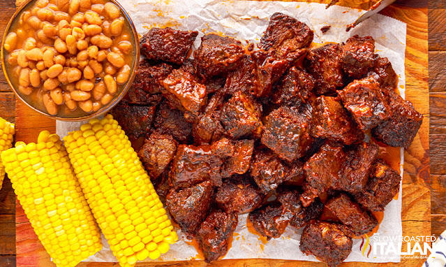cubes of crispy oven roasted beef roast next to bowl of pinto beans and cooked ears of corn