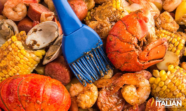 brushing old bay butter over seafood boil ingredients