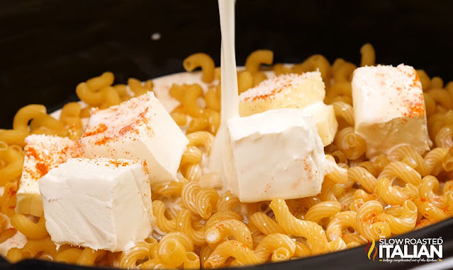pouring milk into slow cooker over corkscrew pasta and cream cheese