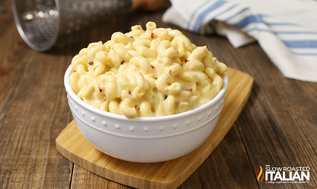 A bowl of mac n cheese sitting on top of a wooden cutting board