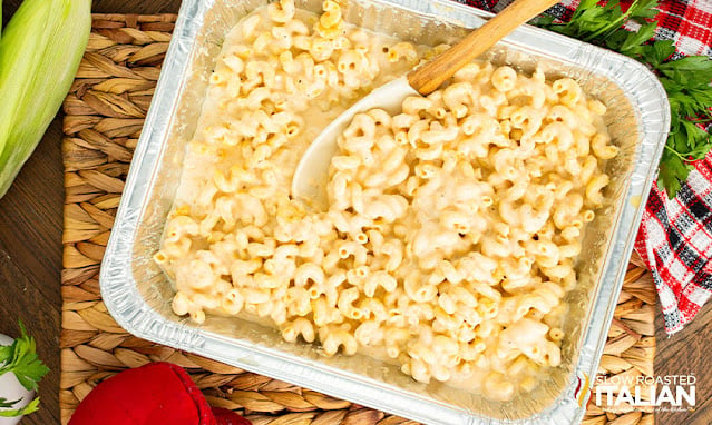 overhead: serving spoon in aluminum foil pan of creamy pasta in cheese sauce