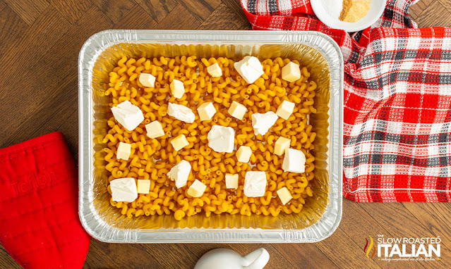 overhead: cubes of cream cheese and butter over elbow macaroni in tinfoil pan