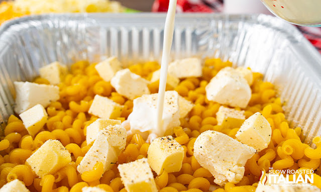 pouring milk into pan of pasta and cream cheese for smoked mac and cheese recipe