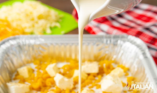 pouring heavy cream into tinfoil pan of raw macaroni