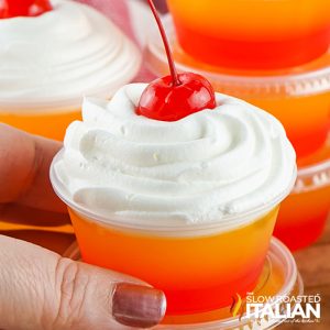 tequila sunrise jello shot topped with whipped cream and maraschino cherry