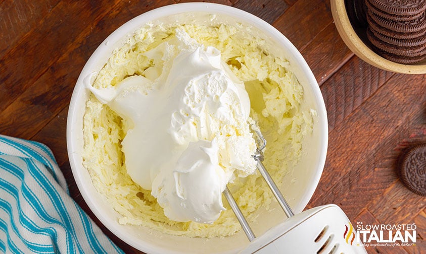 electric hand mixer blending cool whip and cream cheese in mixing bowl