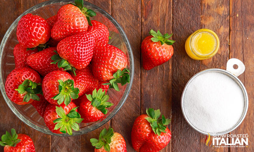 overhead: bowl of red berries next to cup of sugar and lemon juice