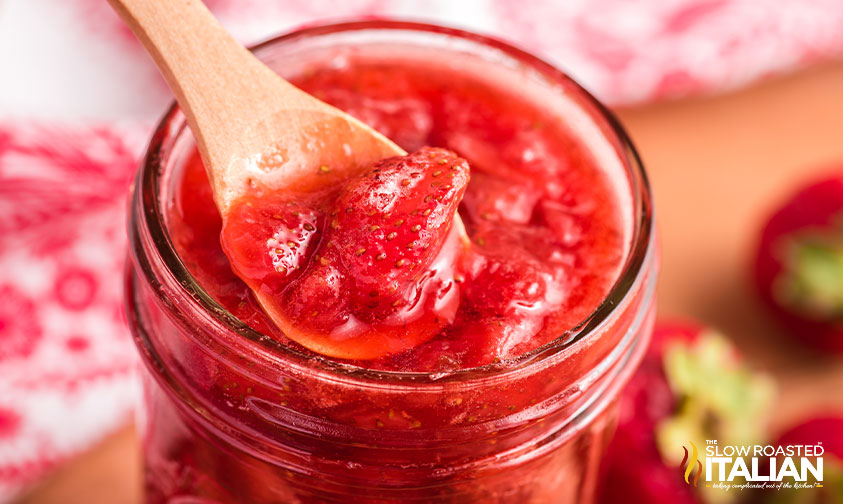 fresh strawberry syrup on wooden spoon above jar