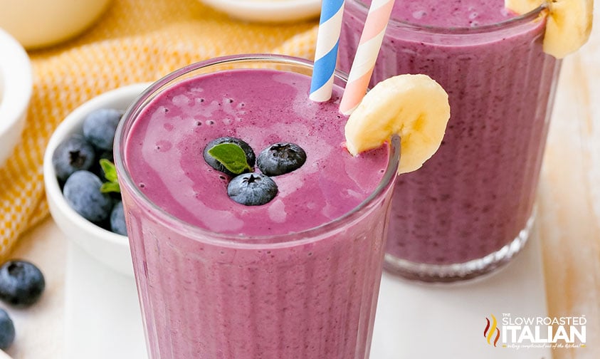 blueberry banana smoothie in glass with straw and fruit garnish