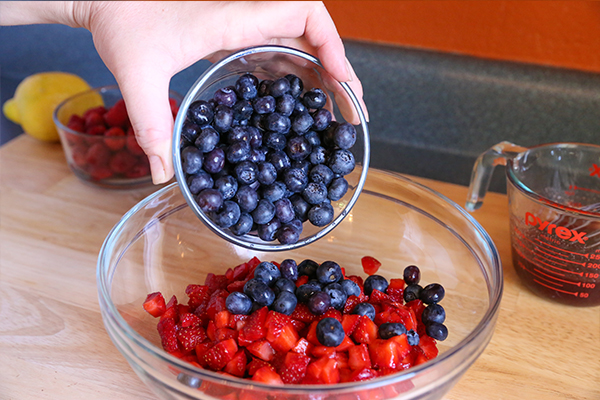 adding fresh blueberries to bowl for summer fruit salad