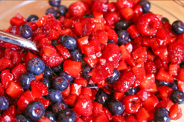 large serving spoon in bowl with chopped fresh raspberries, strawberries and blueberries