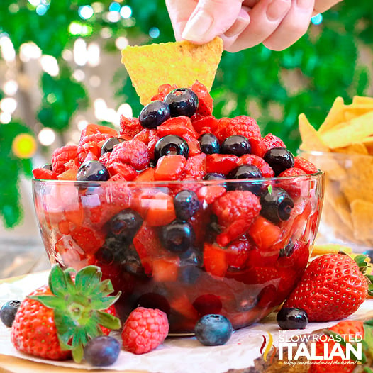 dipping chip into glass bowl of mixed berry fruit salad