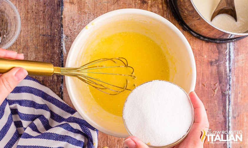 adding sugar to whisked eggs in bowl