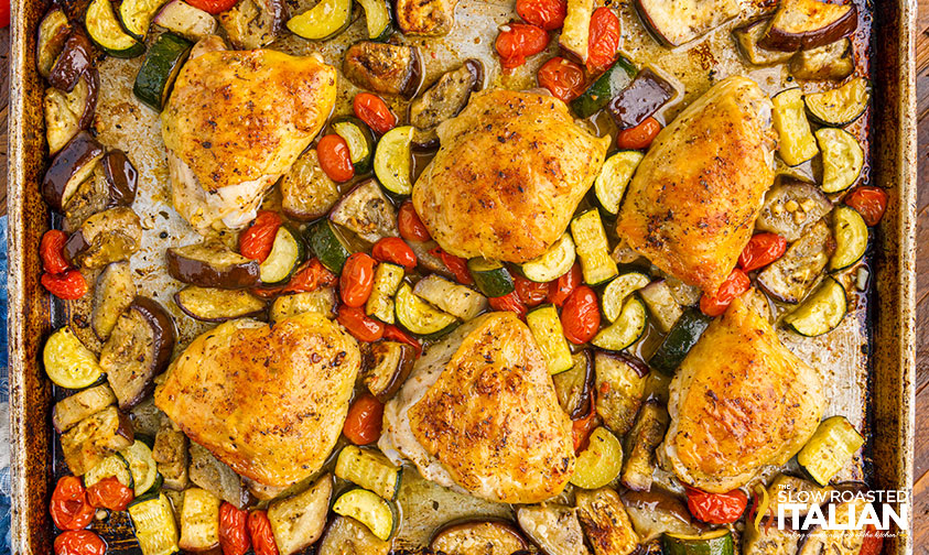 cooked italian chicken thighs and vegetables on baking sheet