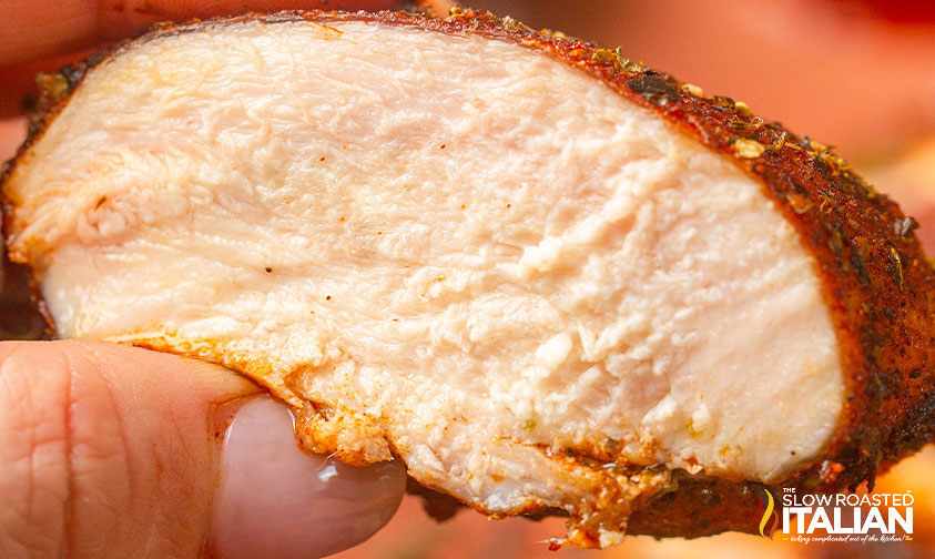 fingers holding a slice of smoked chicken breast