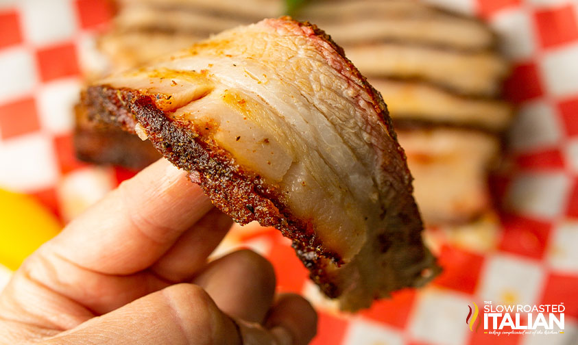 hand holding strip of sliced meat with crispy edges