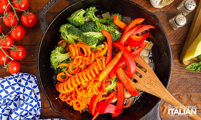 adding fresh veggies to cast iron skillet for healthy pasta primavera