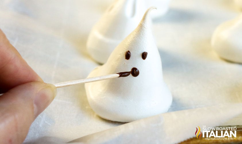 painting face on meringue ghost with melted chocolate