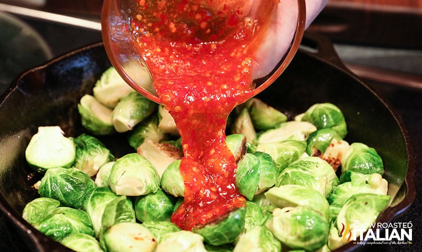 pouring chili sauce on brussels sprouts.