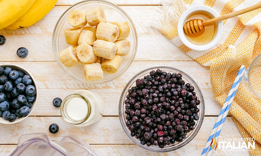 bowls of fresh berries and bananas next to honey and milk