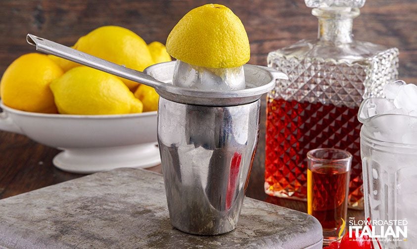 juicer with lemon resting on a cocktail shaker surrounded by amaretto and lemons