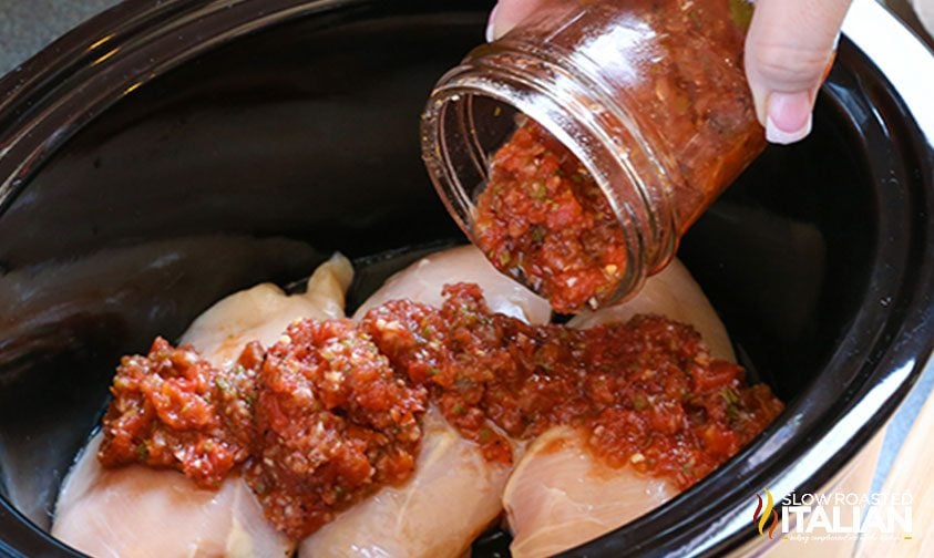 pouring jar of salsa over chicken in crock pot