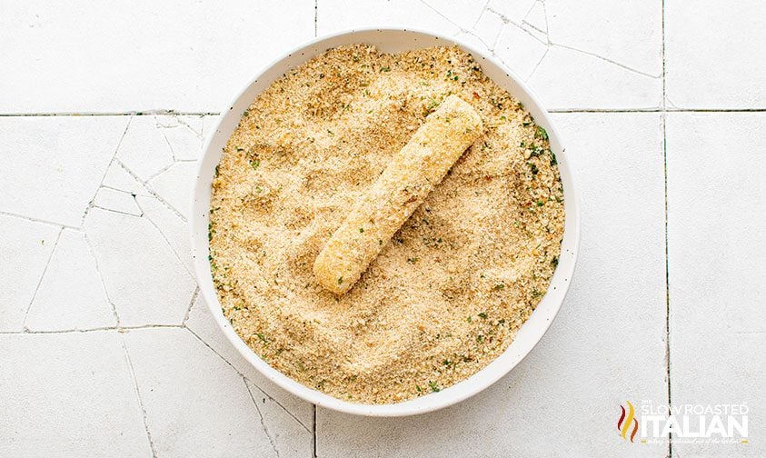 coated cheese stick in bowl of Italian breadcrumbs