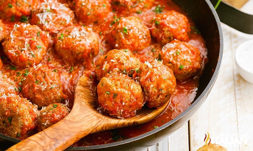 sausage and beef meatballs in red sauce on wooden spoon in skillet