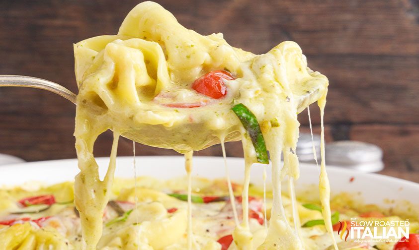 fork scooping pesto tortellini out of a bowl