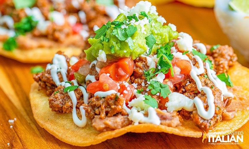 closeup: fried tortilla topped with beef, salsa, guac, sour cream, and cilantro