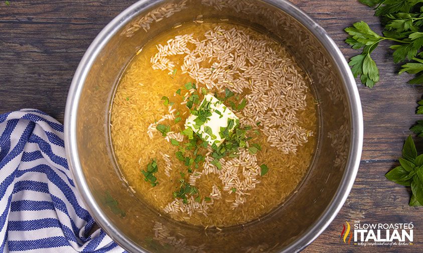 brown rice in pressure cooker with broth, butter, and chopped parsley