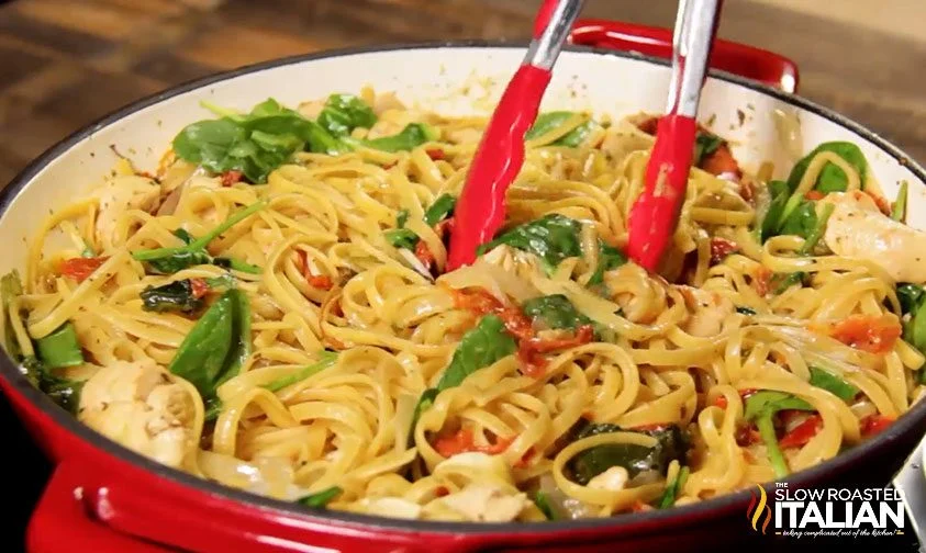 red tongs stirring a pot of cheesy chicken pasta