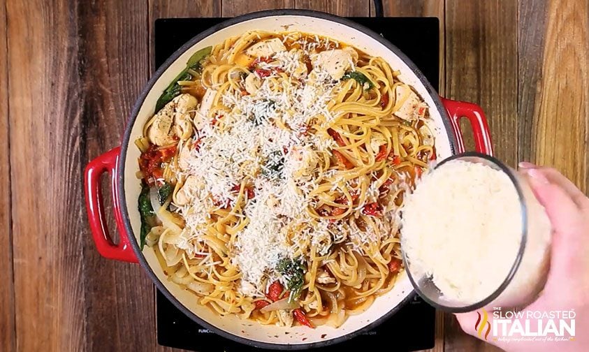 sprinkling shredded cheese over pot of chicken pasta