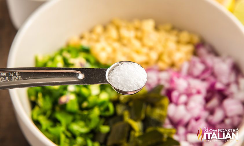 adding salt to bowl of corn salsa ingredients