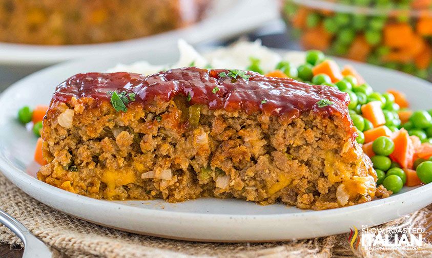 slice of cracker barrel copycat meatloaf on a plate with mashed potatoes and veggies