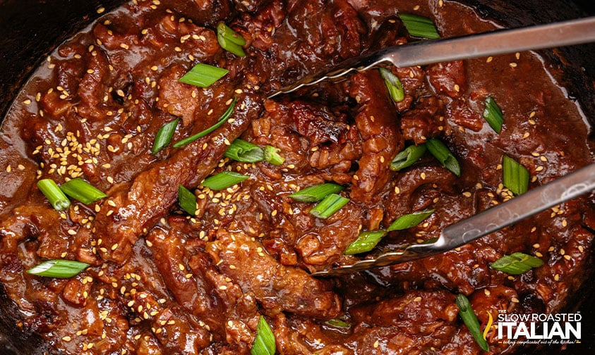 tongs in crock pot of mongolian beef with green onions
